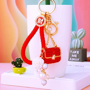Close-up of a red woven rope keychain with mini rhinestone handbag and pearl charms