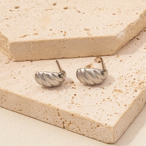 Macro view of textured 304 stainless steel earrings on beige travertine stone blocks