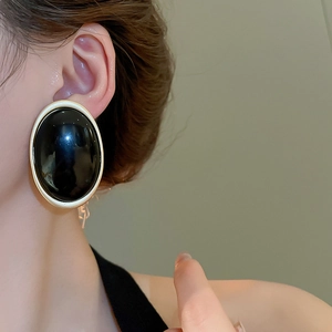 Gros plan d'un mannequin portant des boucles d'oreilles ovales noires avec cadre doré