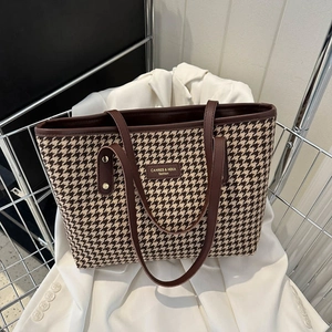 Vintage houndstooth tote bag with brown leather handles placed on a white suit jacket