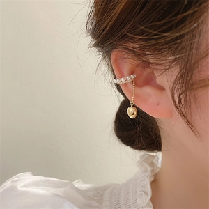 Dettaglio di un ear cuff dorato con perle delicate e un ciondolo a forma di cuore