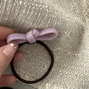 Close-up of a pink ceramic texture bow hair tie held against a beige woven background