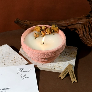 Handmade scented candle in pink ceramic jar with dry rose buds on a stone background