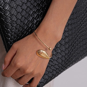 Detailed view of a gold-plated teardrop bangle worn on a model with leather background