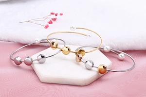 Three-color cable wire bangles set with imitation pearls on a white stone display pedestal