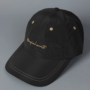 Close-up of black plaid baseball cap with golden Magical secrets cursive embroidery