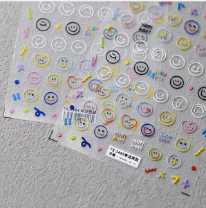 Dettaglio di adesivi 3D in rilievo per unghie con sorrisi colorati e motivi portafortuna