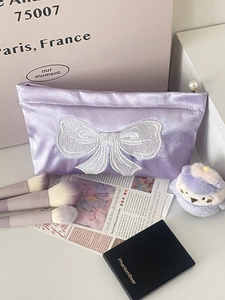 Close-up of purple satin cosmetic bag with bow embroidery and pearl zipper detail