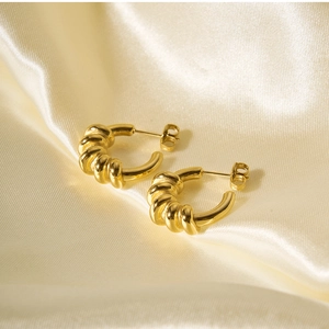 Detail shot of spiral hoop earrings in 18k gold plating on beige silk background