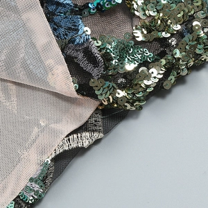 Détail de broderie avec paillettes vertes et motifs floraux bleus sur résille noire