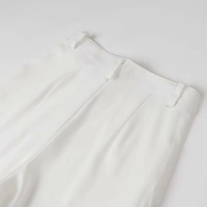 Detailed view of the white satin trousers waistline featuring precise tailoring and belt loops