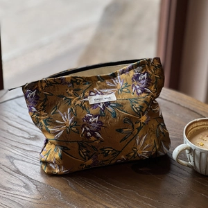 Close-up of caramel jacquard floral makeup bag with simple wish label on a wooden table