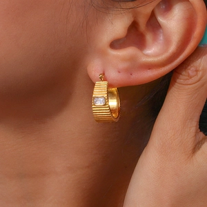 Detailed close-up of a gold-plated chunky C-hoop earring with horizontal textures and zircon