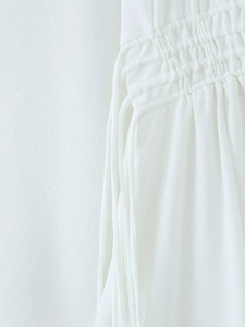 Macro detail of white smocked fabric and side tie strings on this V-neck long dress