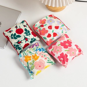 Close-up of four floral print fabric tote bags with zippers on a white desktop