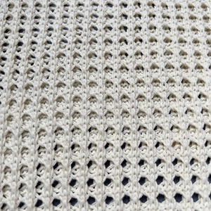 Close-up detail of cream white hollow out knitted fabric with diamond mesh texture
