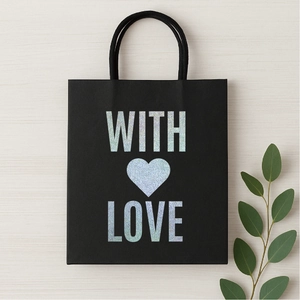 Black gift bag with silver glitter 'WITH LOVE' text and heart on beige wood background