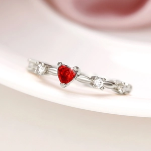 Macro detail of silver heart ring with red zircon and wave design with white stones
