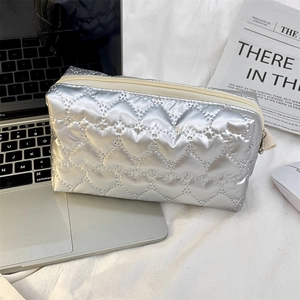 Close-up of a silver quilted makeup bag with metallic finish next to a laptop and newspaper