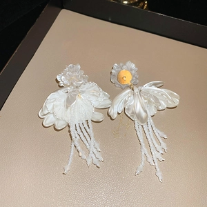 Detailed macro view of white flower tassel earrings with crystals on a beige tray