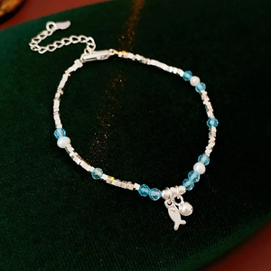 Close-up of pearl and blue beaded bracelet with silver fish charms on green velvet