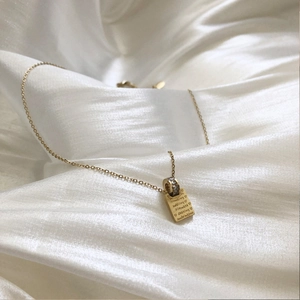 Collana in acciaio dorato con pendente quadrato inciso e anello di zirconi su seta bianca