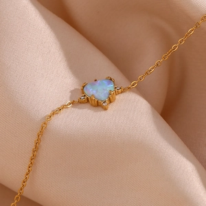 Detailed close-up of heart-shaped opal pendant on golden chain over silk fabric