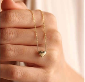 Polished gold 3D heart pendant necklace shown delicately wrapped around a model's hand