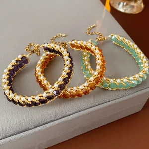 Detailed view of woven pearl and crystal bracelets in purple, amber and mint on velvet box
