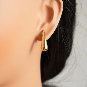 Detailed view of polished gold teardrop earrings worn by a model on the ear