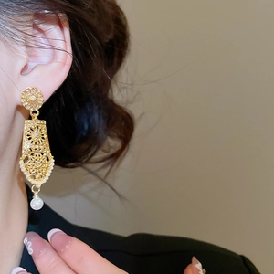 Detailed close-up of vintage hollow gold earrings with pearls on a model's ear