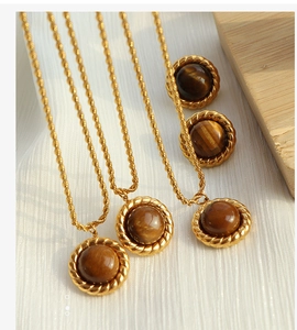Detailed shot of tiger eye jewelry set with golden twisted chain on white textured fabric