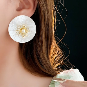 Nahaufnahme eines runden weißen Ohrrings mit goldenem Sonnenstrahl und Perle