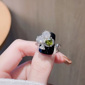 Detail of silver clover ring featuring a green heart gem and zircon inlay on hand