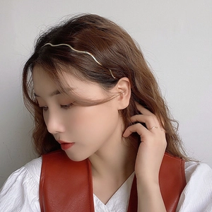 Detail of a wave-shaped gold metal headband worn by a model with a minimalist ring