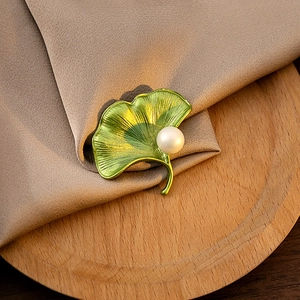 Close-up of green ginkgo leaf brooch with pearl on silk fabric and wooden board
