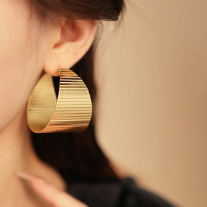 Macro shot of large gold wide hoop earring with textured horizontal stripe finish