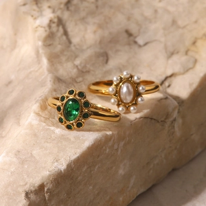 Close-up of luxury gold rings featuring emerald and pearl oval gemstones on stone base