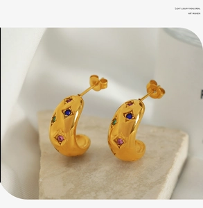Detail of gold C-shaped hoop earrings with colorful starburst-set crystals on stone