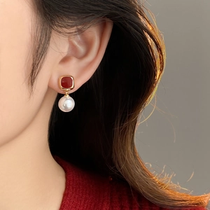 Detail of red square stud and round white pearl drop earring worn by a model