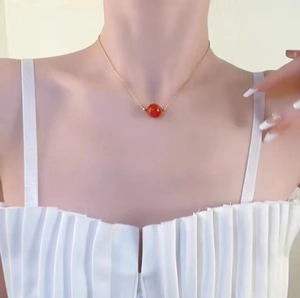 Detailed close-up of a red agate bead on a gold snake chain worn by a female model