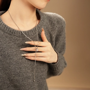 Detail of silver Y-shaped necklace with crystal pendant on a grey sweater