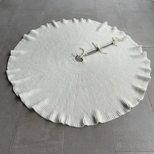 Detailed top view of a white knitted Christmas tree skirt with ribbon ties on a floor