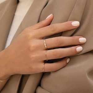 Close-up of three gold rings on model hand featuring wide band and chain link designs