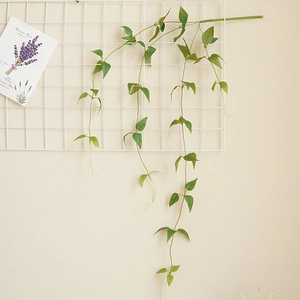 Artificial clematis vine with green leaves hanging on a white wall grid for home decor