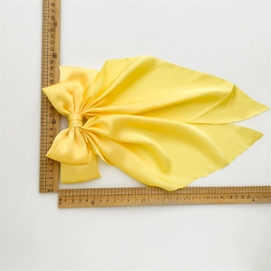 Macro detail of silk-like yellow bow hairclip with long ribbons and size measurements
