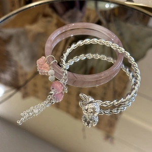 Detail of pink jade bangle paired with silver twist bracelet featuring a rabbit charm