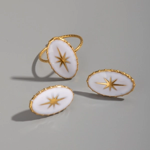 Détail de boucles d'oreilles ovales et bague avec motifs d'étoiles dorées sur émail blanc