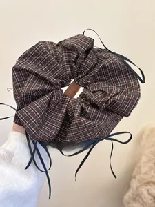 Detail of plaid scrunchie with black bows held by a hand over a soft white sweater