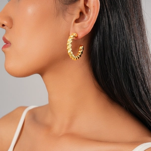 Close-up of golden twisted rope texture hoop earrings worn on a model for scale